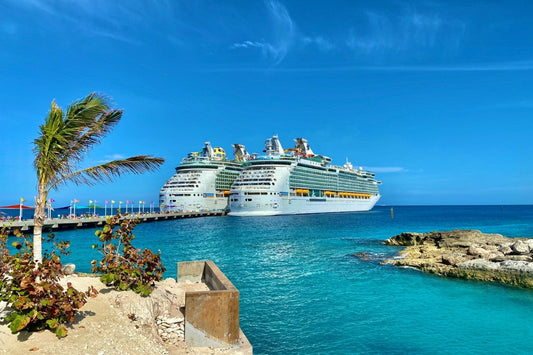 Two Royal Caribbean–style cruise ships at a Caribbean pier under clear blue skies, peak season port scene.